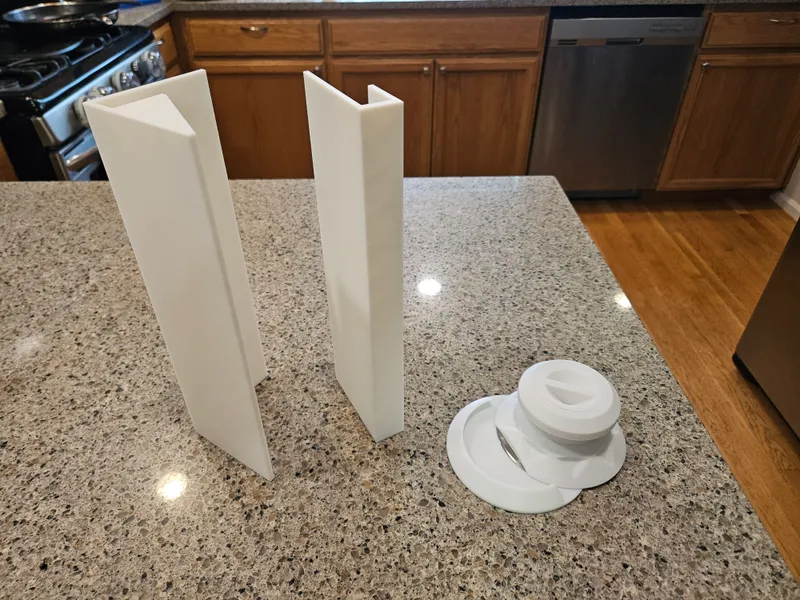A pair of white 3D-printed plough and press attachments standing upright on a countertop, next to a round threaded knob